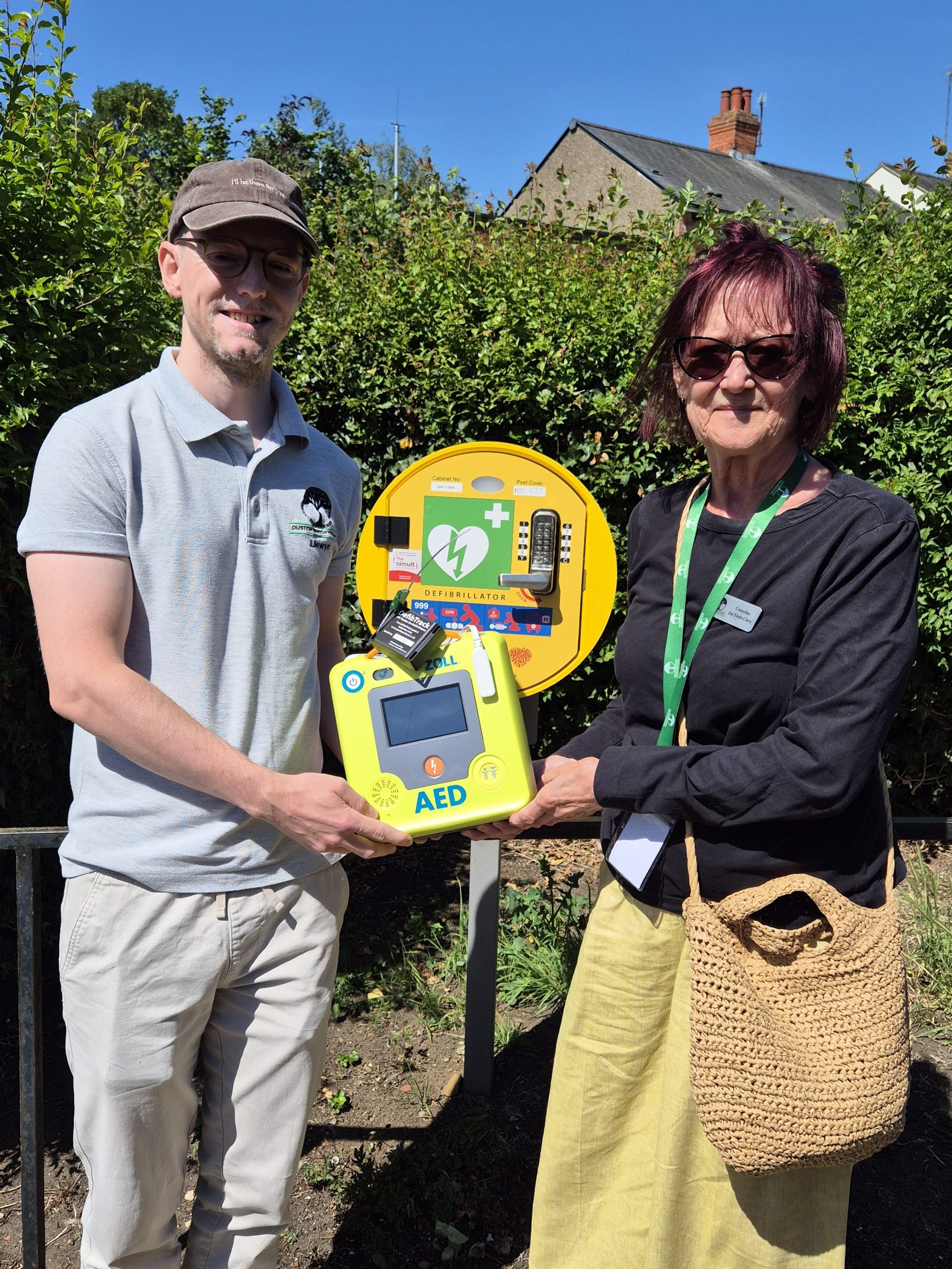 Duston Village Hall Defib station close-up with Turtle Medical’s DefibTrack installed to the defibrillator. The emergency defib cabinet at Duston Village Hall containing a defibrillator fitted with DefibTrack. L to R - Llewyn Mitchell, Duston Parish Council’s Estate Officer and Chair of the Parish Council, Jan Ennis-Clark